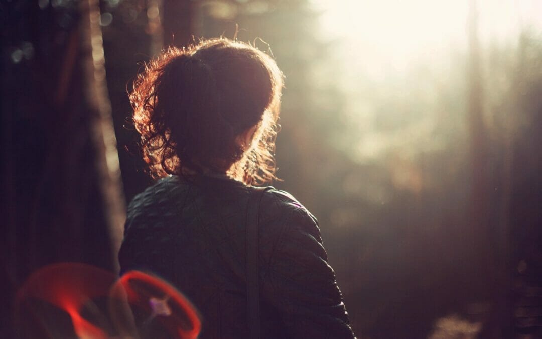 woman sitting looking towards light in forest